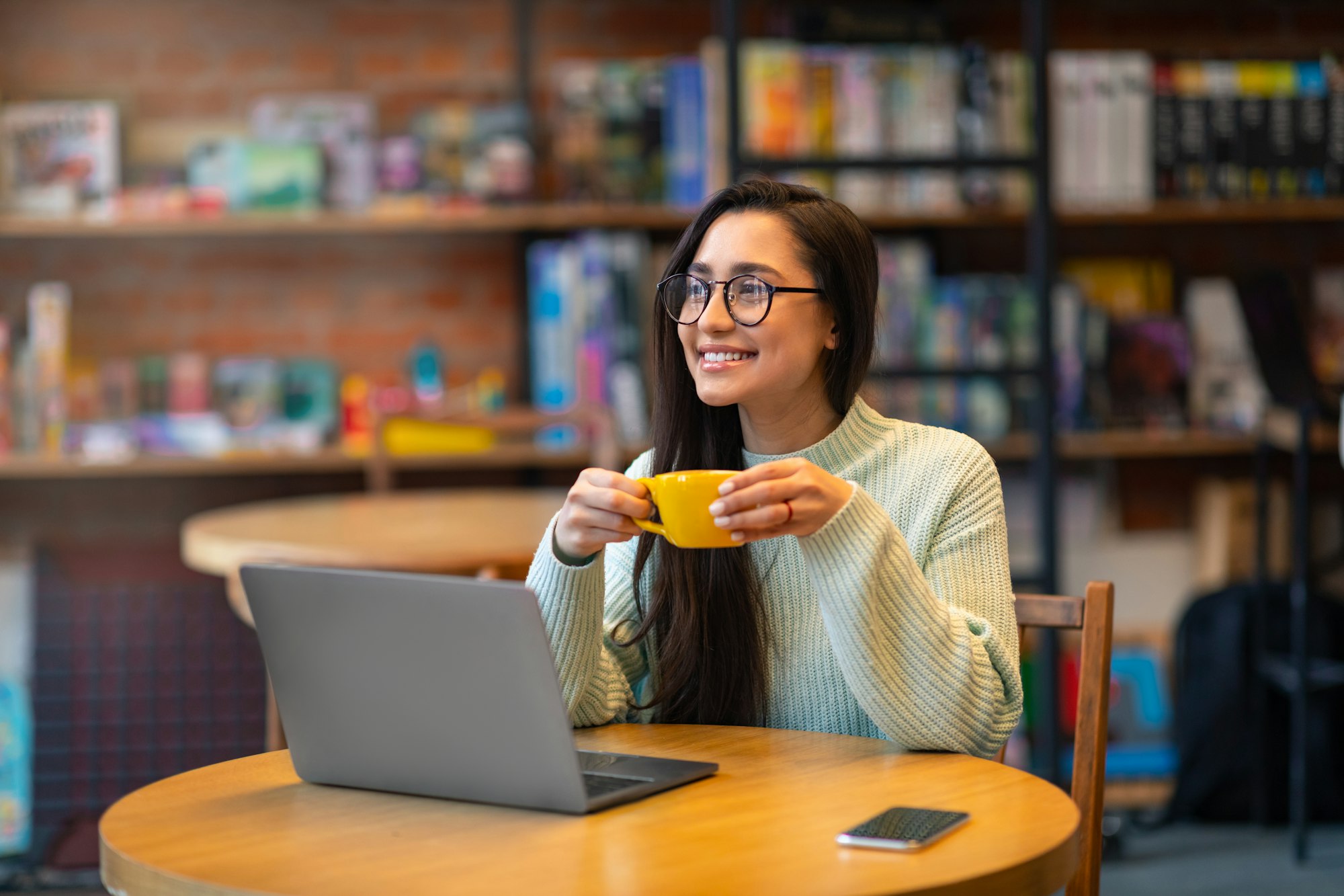 Carefree latin woman working distantly on laptop computer, sitting at cafe and enjoying coffee, free